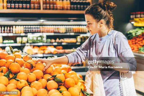 woman choosing orange at market and using reusable eco bag. - female supermarket stock pictures, royalty-free photos & images