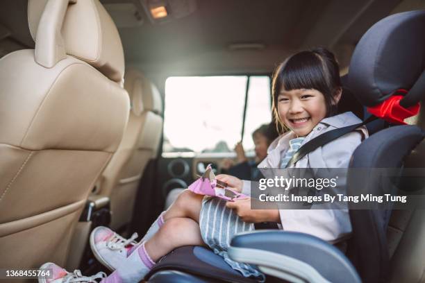 lovely little girl smiling joyfully at the camera while sitting in child car seat, enjoying her snack in the car - child car seat stock pictures, royalty-free photos & images