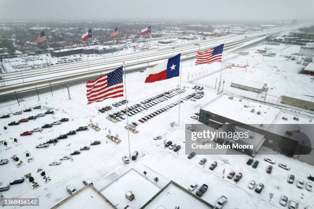 In an aerial view, U.S. And Texas state flags fly over car dealerships as light traffic moves through snow and ice on U.S. Route 183 on February 03,...