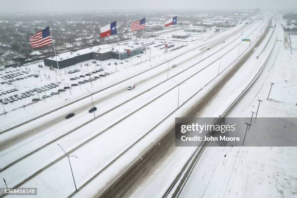 In an aerial view, U.S. And Texas state flags fly over a Nissan car dealership as light traffic moves through snow and ice on U.S. Route 183 on...