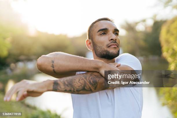 athlete stretching in public park at sunset - man tatoo bildbanksfoton och bilder