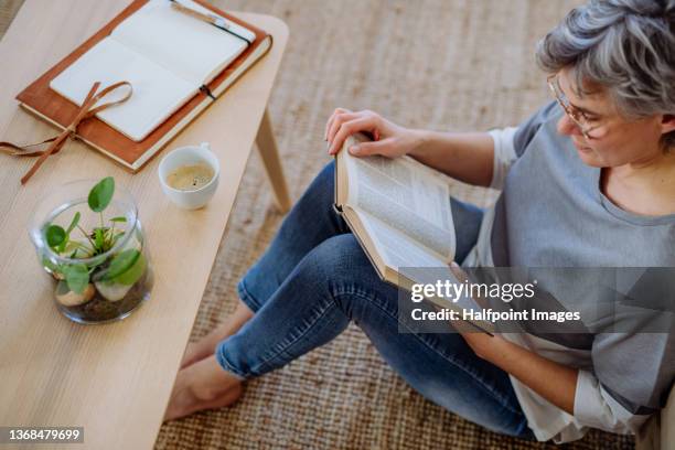 high angle view of mature woman sitting on floor and reading a book at home. - reading glasses top view stock pictures, royalty-free photos & images