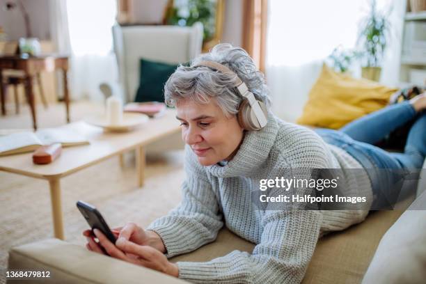 mature woman lying on sofa and listening to music from headphones at home. - ligga på mage bildbanksfoton och bilder