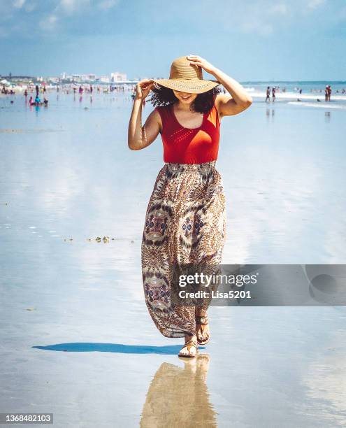 glückliche stilvolle frau, die einen strandurlaub in einem fließenden rock mit sonnenhut genießt - cocoa beach stock-fotos und bilder