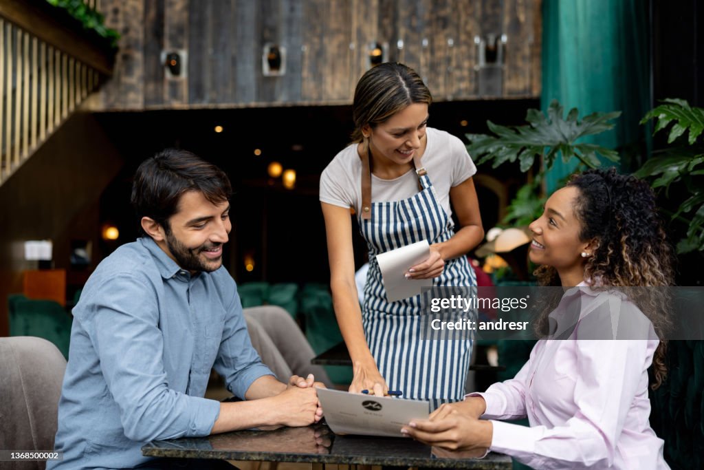 Kunden in einem Restaurant, die der Kellnerin Fragen zum Menü stellen