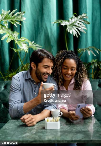 happy millennials looking at social media while drinking coffee at a cafe - coffee shop couple stock pictures, royalty-free photos & images