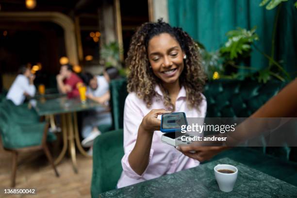 woman making a contatcless payment at a restaurant - paying for dinner imagens e fotografias de stock