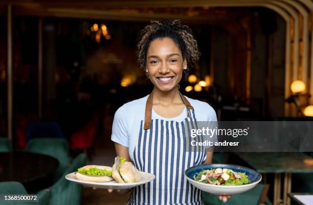 happy waitress serving food while working at a restaurant - waitress bildbanksfoton och bilder