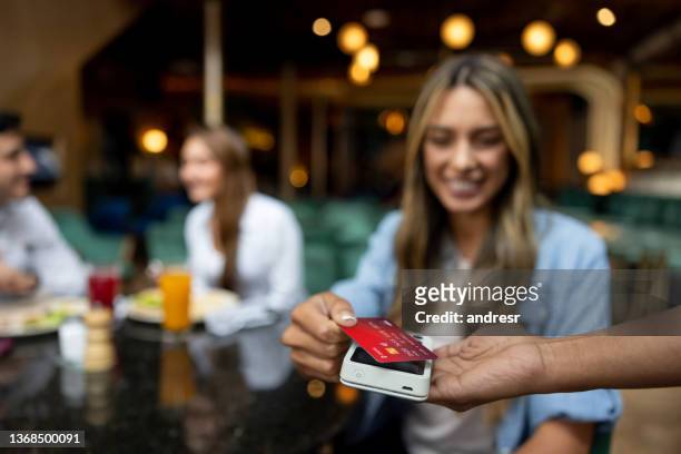 woman making a contactless payment at a restaurant - paying for dinner imagens e fotografias de stock