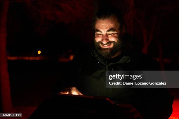 cheerful male browsing tablet in dark park - schwache beleuchtung stock-fotos und bilder