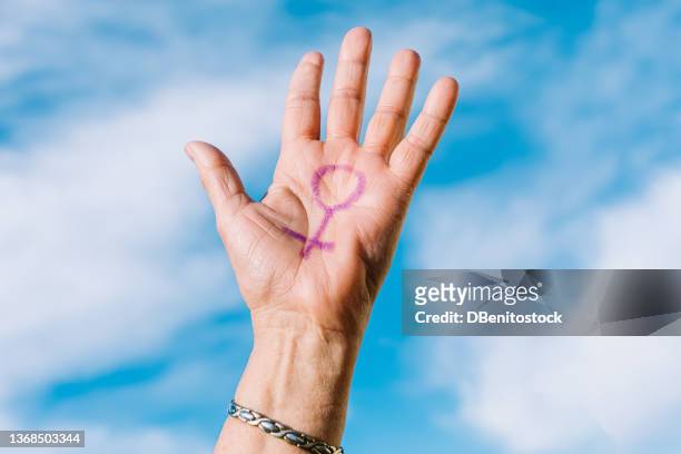 palm of the hand of an older woman in the sunlight with the sky in the background with the female symbol painted in purple. concept of women's day, empowerment, equality, inequality, activism and protest. - colors against violence in madrid stockfoto's en -beelden