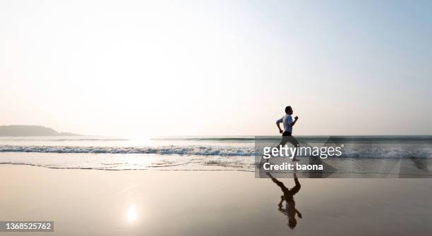 uomo che fa jogging sulla spiaggia al tramonto - asian man barefoot foto e immagini stock
