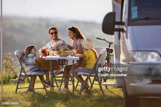happy man playing a guitar to his family during camping day by the trailer. - camping trailer stock pictures, royalty-free photos & images