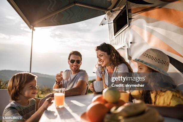 happy family talking at picnic table by the camper trailer in nature. - family caravan stockfoto's en -beelden