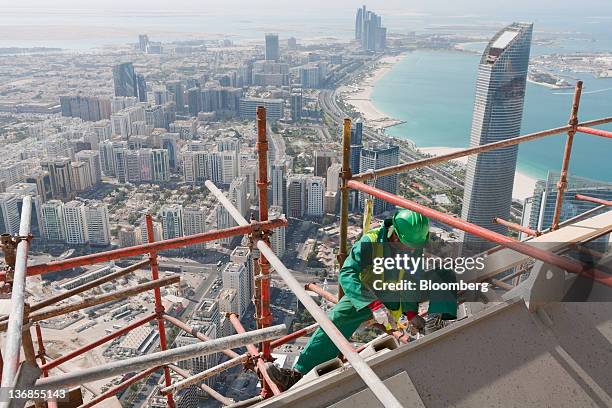 Worker secures scaffolding on a residential tower construction above the Central Market, an Aldar PJSC project, in Abu Dhabi, United Arab Emirates,...