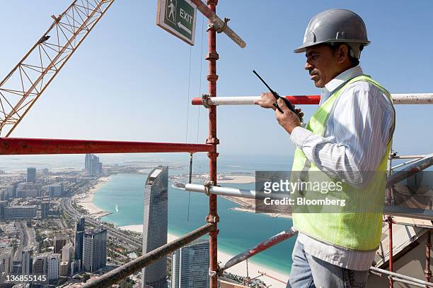 Worker communicates by radio from scaffolding above a Central Market residential tower, an Aldar PJSC project, under construction in Abu Dhabi,...