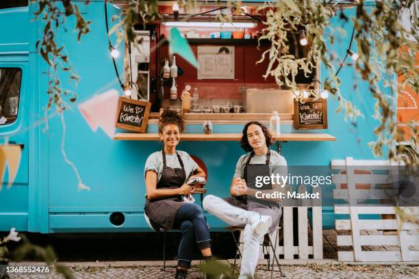 smiling male and female entrepreneurs sitting outside food truck - streetfood stock-fotos und bilder