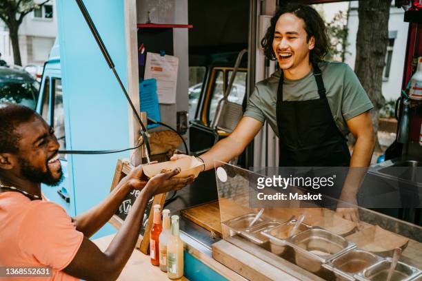 male owner giving food container to laughing customer - furgón de comida fotografías e imágenes de stock
