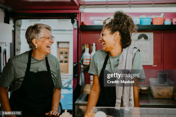 female owner and coworker laughing in food truck kitchen - einzelhandelsberuf stock-fotos und bilder