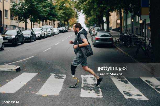 side view of mature man with prosthetic leg jogging on street in city - körperliche behinderung stock-fotos und bilder