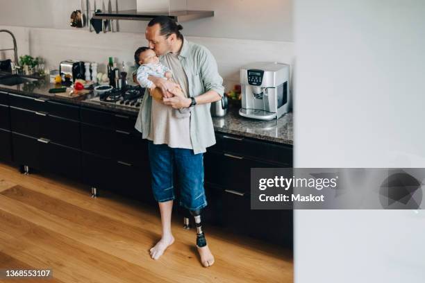 disabled father kissing son while standing in kitchen - disabilitycollection fotografías e imágenes de stock