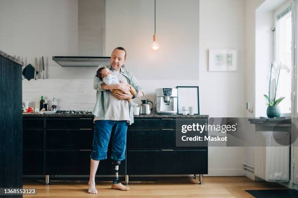 father carrying son standing in kitchen at home - amputee home stock pictures, royalty-free photos & images