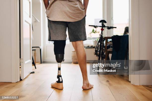 low section rear view of man with prosthetic leg standing at home - prothese stock-fotos und bilder