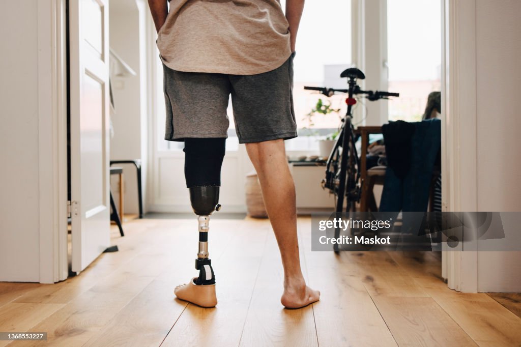 Low section rear view of man with prosthetic leg standing at home