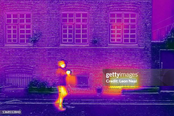 In this image made with a thermal camera, a person walks past windows showing signs of heat loss on February 04, 2022 in London, England. The energy...