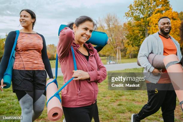 smiling male and female with exercise mats walking in park - yoga outdoor foto e immagini stock