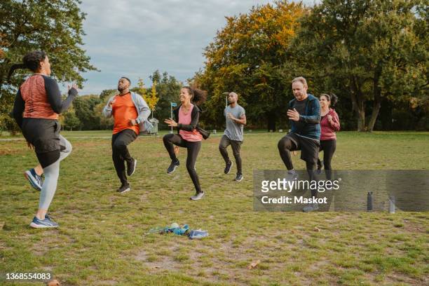 female instructor teaching running exercise to men and women in park - sport stock-fotos und bilder
