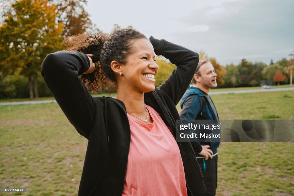 Cheerful woman tying hair by male friend in park