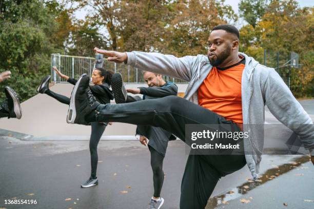 multiracial male and female friends doing warm up exercise in park - fitness vitality wellbeing stockfoto's en -beelden