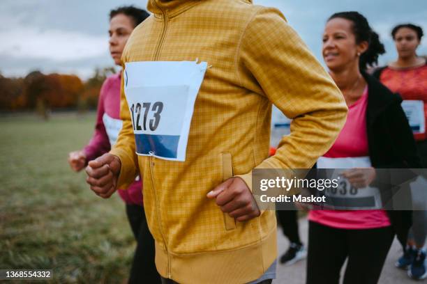 male and female friends running together in park - bib stock pictures, royalty-free photos & images