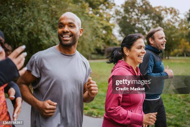 cheerful male and female friends running at park - germany womens training stockfoto's en -beelden