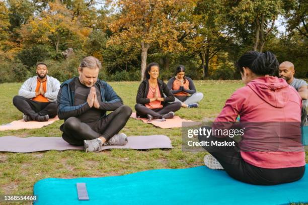 female instructor teaching meditation to men and women during exercise class in park - yoga germany stockfoto's en -beelden