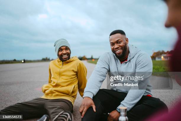 smiling male friends sitting together in park - depth of field togetherness looking at the camera stock pictures, royalty-free photos & images