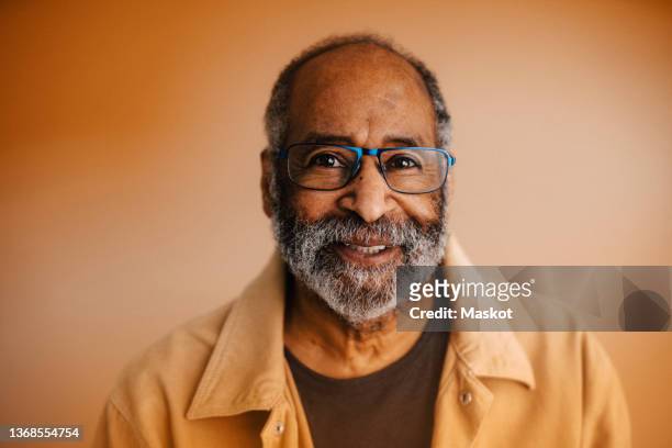 portrait of smiling senior man against brown background - formal portrait stockfoto's en -beelden