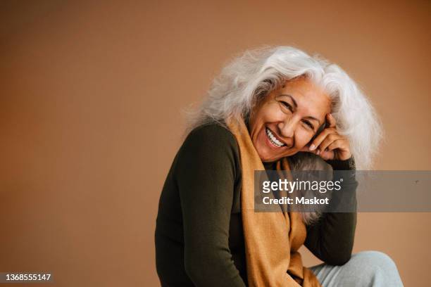 cheerful elderly woman with head in hand over brown background - woman studio stock pictures, royalty-free photos & images