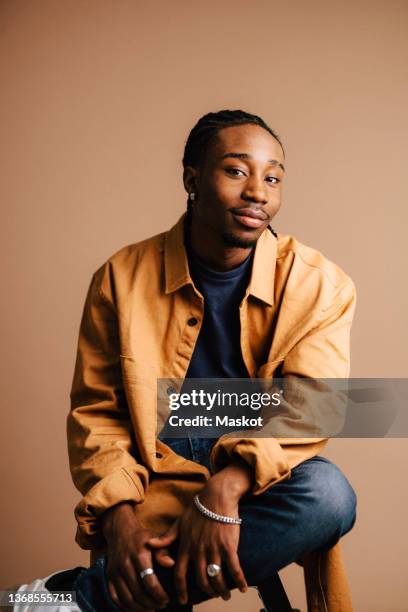 young man with legs crossed sitting in studio - mens casual clothing stock pictures, royalty-free photos & images