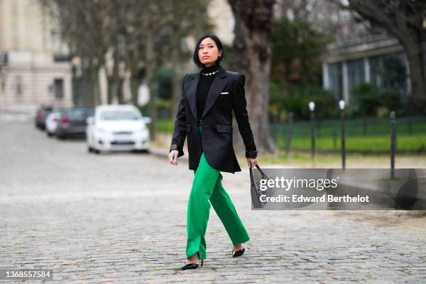 Miki Cheung wears large silver and rhinestones / crystals earrings, a silver with crystal necklace, a black ribbed turtleneck ribbed pullover, a...