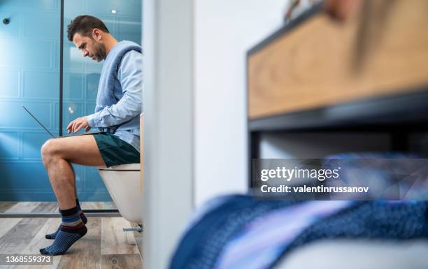 young man with shirt, sitting on the toilet, holding laptop on his knees and having online conversation in a difficult situation - men taking a dump stock pictures, royalty-free photos & images