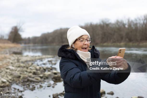 senior woman enjoying the outdoors, video chatting on mobile phone - in ear headphones stock pictures, royalty-free photos & images