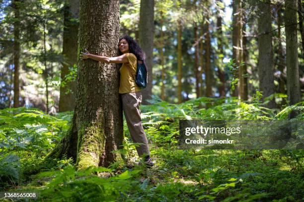 seitenansicht einer reifen frau, die einen baum im wald umarmt - einen baum umarmen stock-fotos und bilder