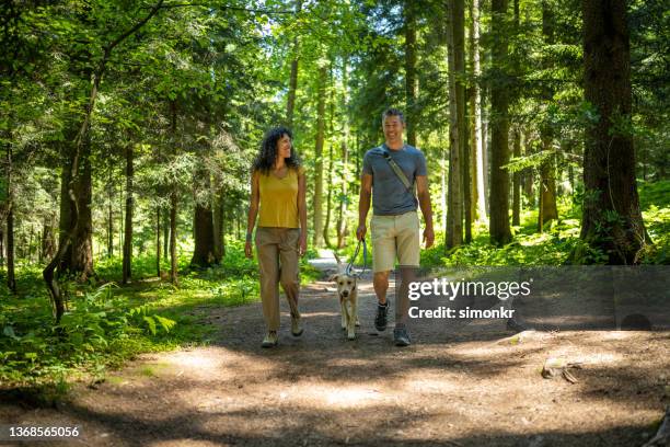 pareja madura caminando por una pista de tierra en el bosque - two men one woman fotografías e imágenes de stock