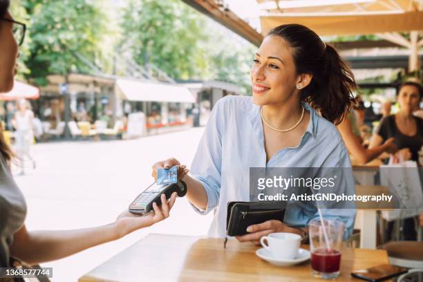 mujer sonriente en un café pagando con su tarjeta. - carta fotografías e imágenes de stock