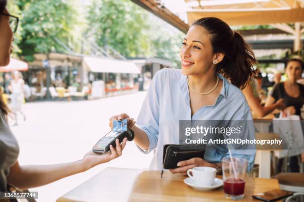 smiling woman on a cafe paying with her card. - 付錢 個照片及圖片檔