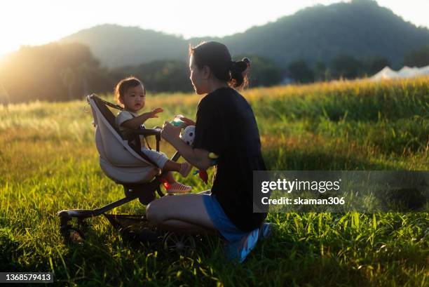 happiness togetherness mother  pushing baby stroller with her daughter leisure outdoor against sunlight sunset time at countryside - baby pram in the park stock-fotos und bilder