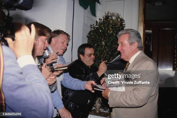 British actor Patrick Macnee wearing a tan suit in conversation with people as he attends an event at the Friars Club of Beverly Hills in Beverly...