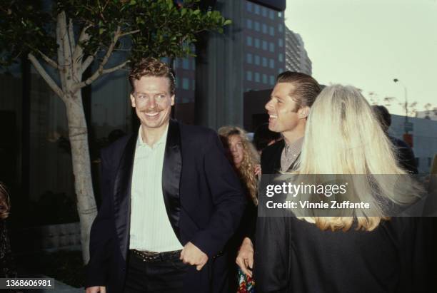 American actor Christopher McDonald, wearing a tuxedo with a white shirt, open at the collar, with people, 1990.